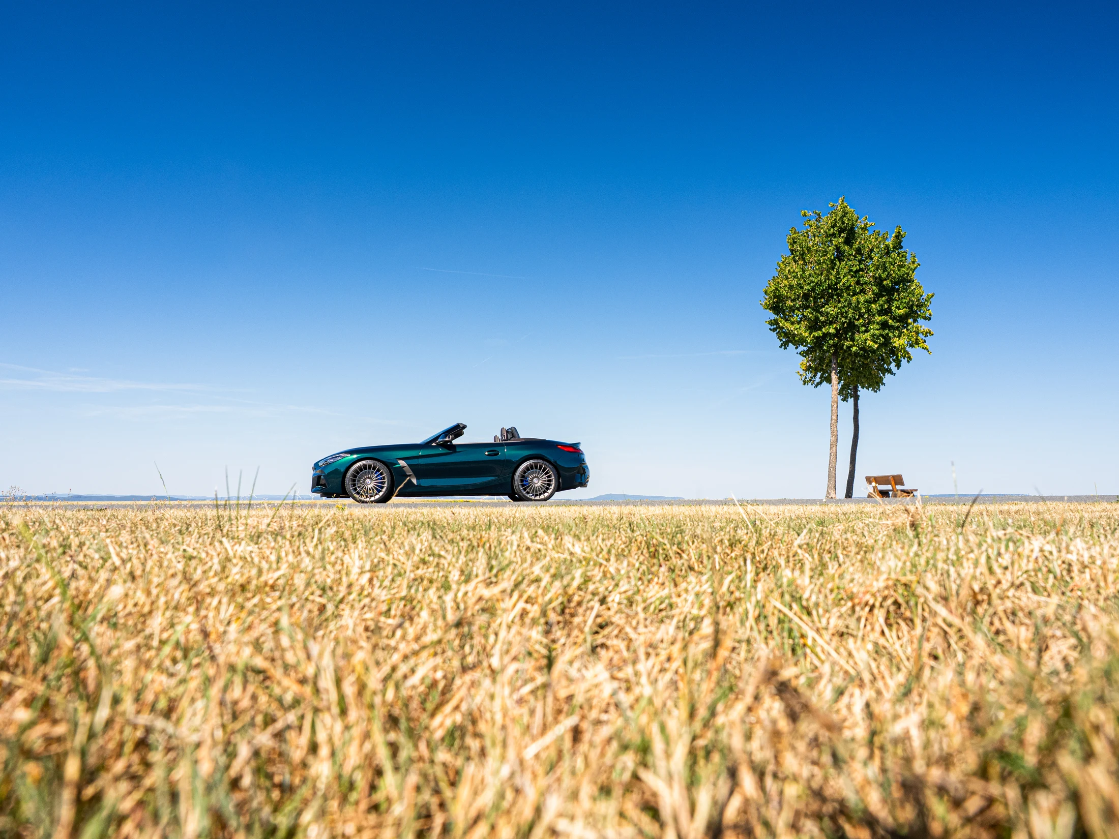 Petrolgrüner Leggera in Seitenansicht hinter einem goldenen Feld unter blauem Himmel